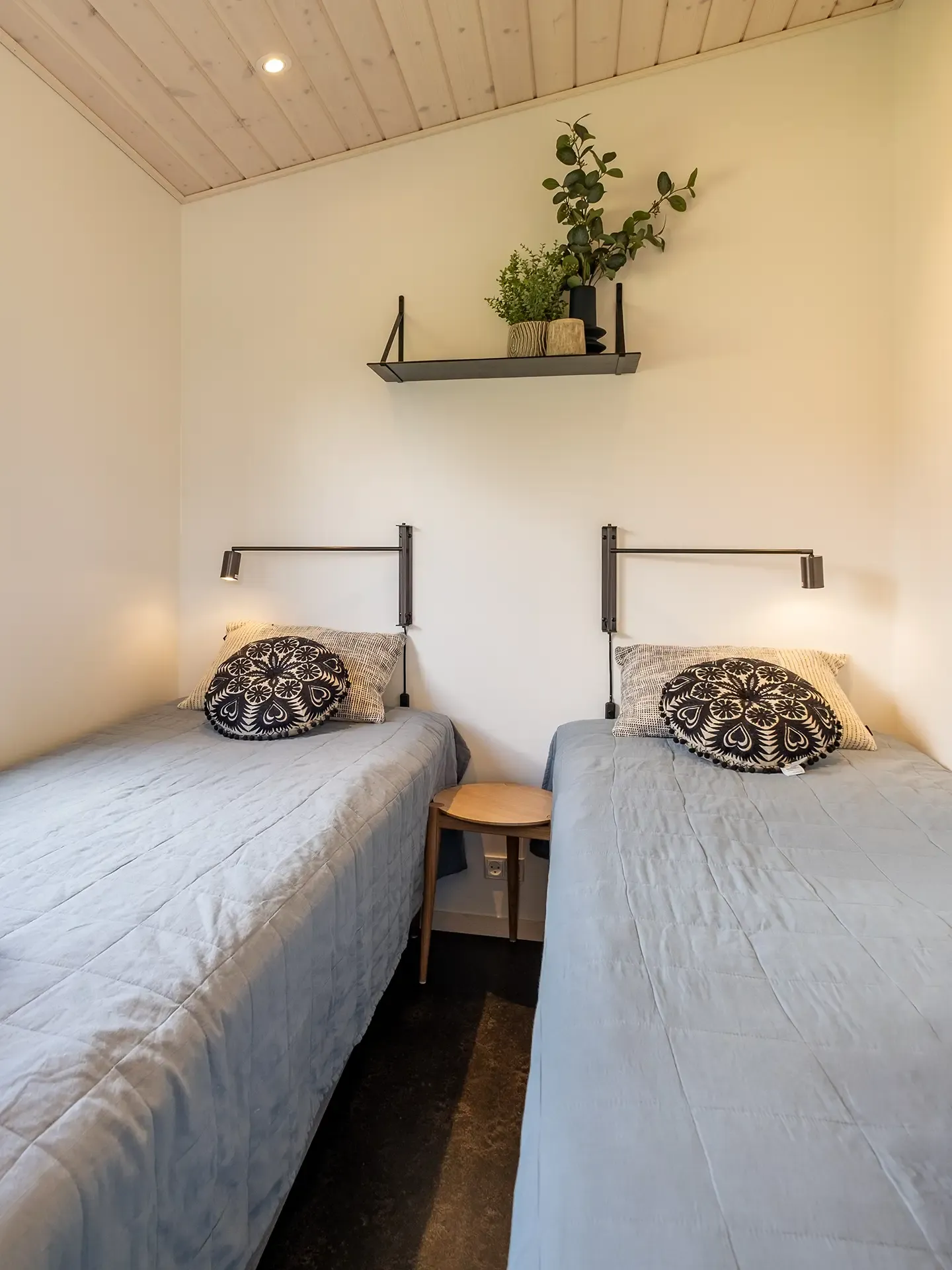 Cozy twin bedroom in Scandinavian camping cabin, featuring minimal Nordic decor, soft bedding, and wall-mounted reading lights – perfect for holiday park furnishing.