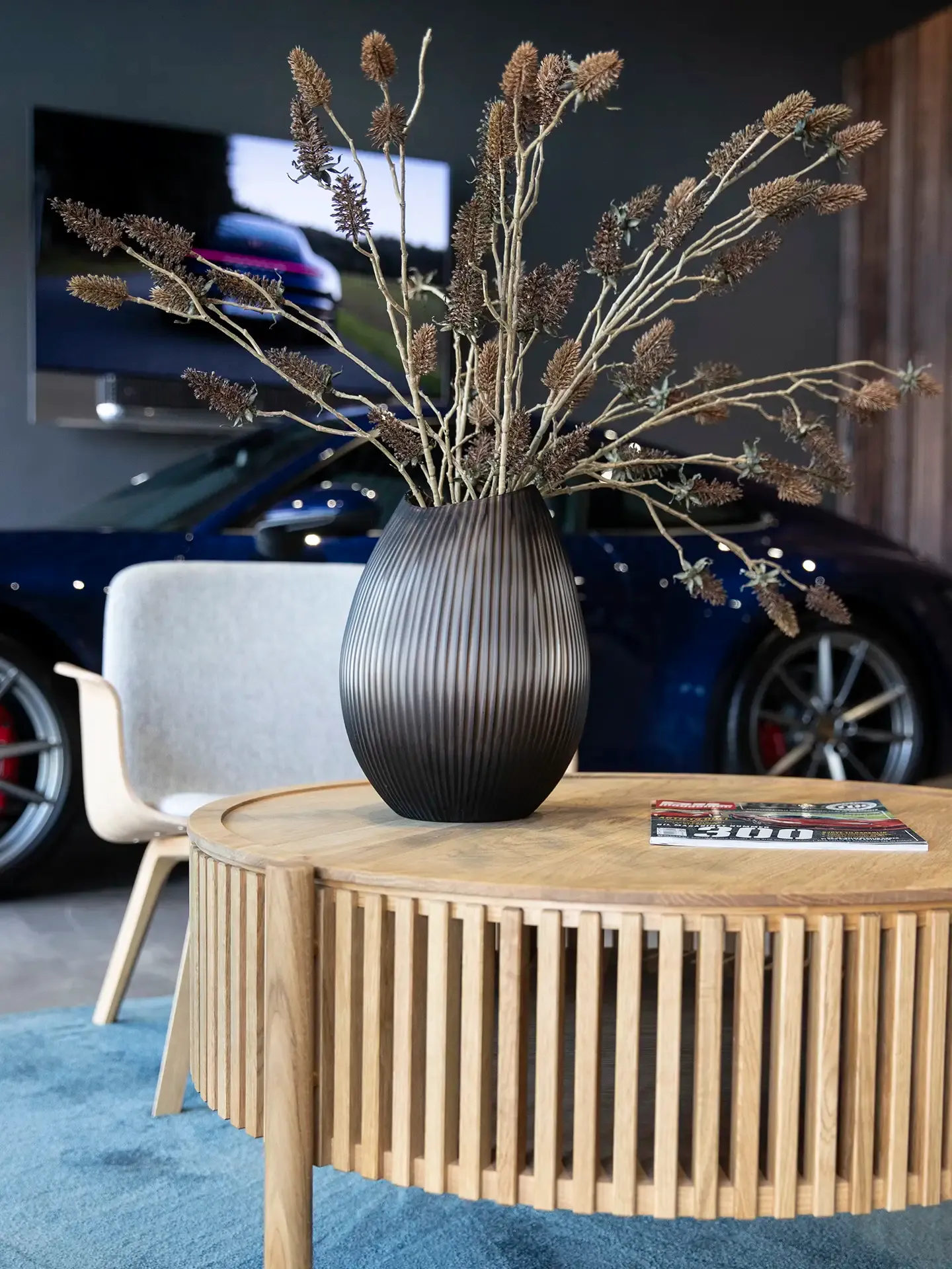 Exclusive showroom corner with Bolia lounge chair, oak side table, and sports car display in the background.