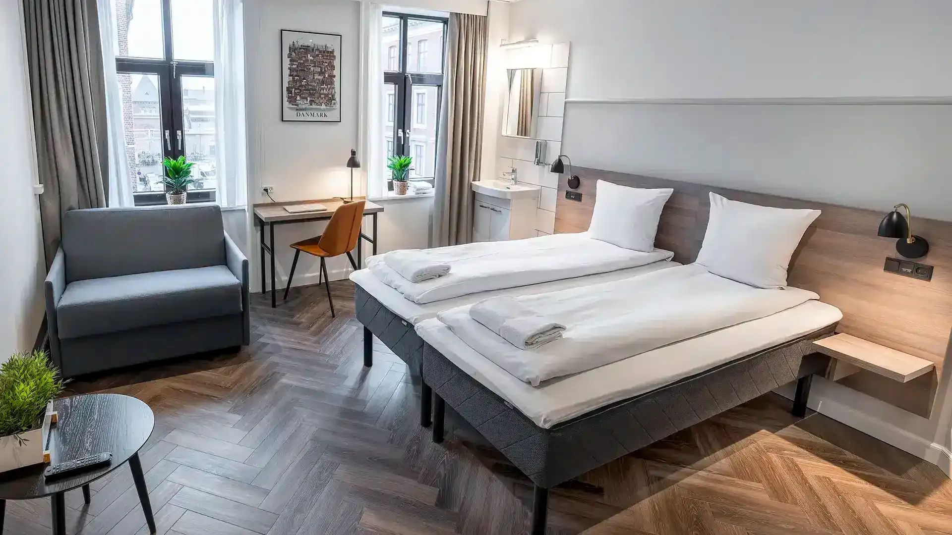Hotel room with twin beds and soft grey lounge chair, Scandinavian design expression.