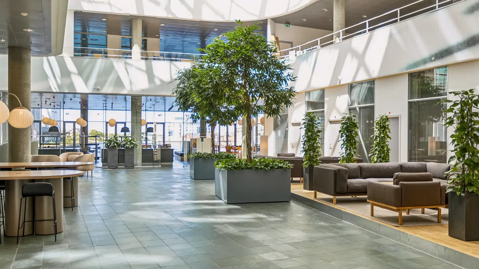 Spacious foyer lounge with natural light, greenery and modular seating for modern corporate headquarters.