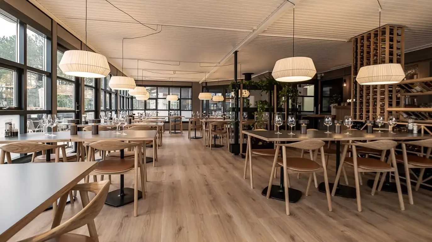 Spacious Nordic-style restaurant with large windows, oak furniture and natural lighting – suitable for modern resort interiors and shared guest spaces.