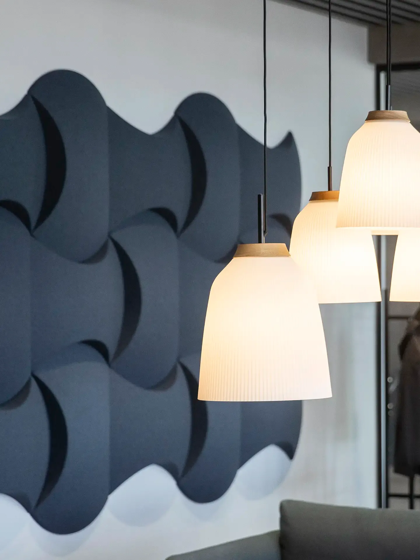 Glass and oak pendant lamps with blue felt acoustic panels in a modern showroom meeting area.