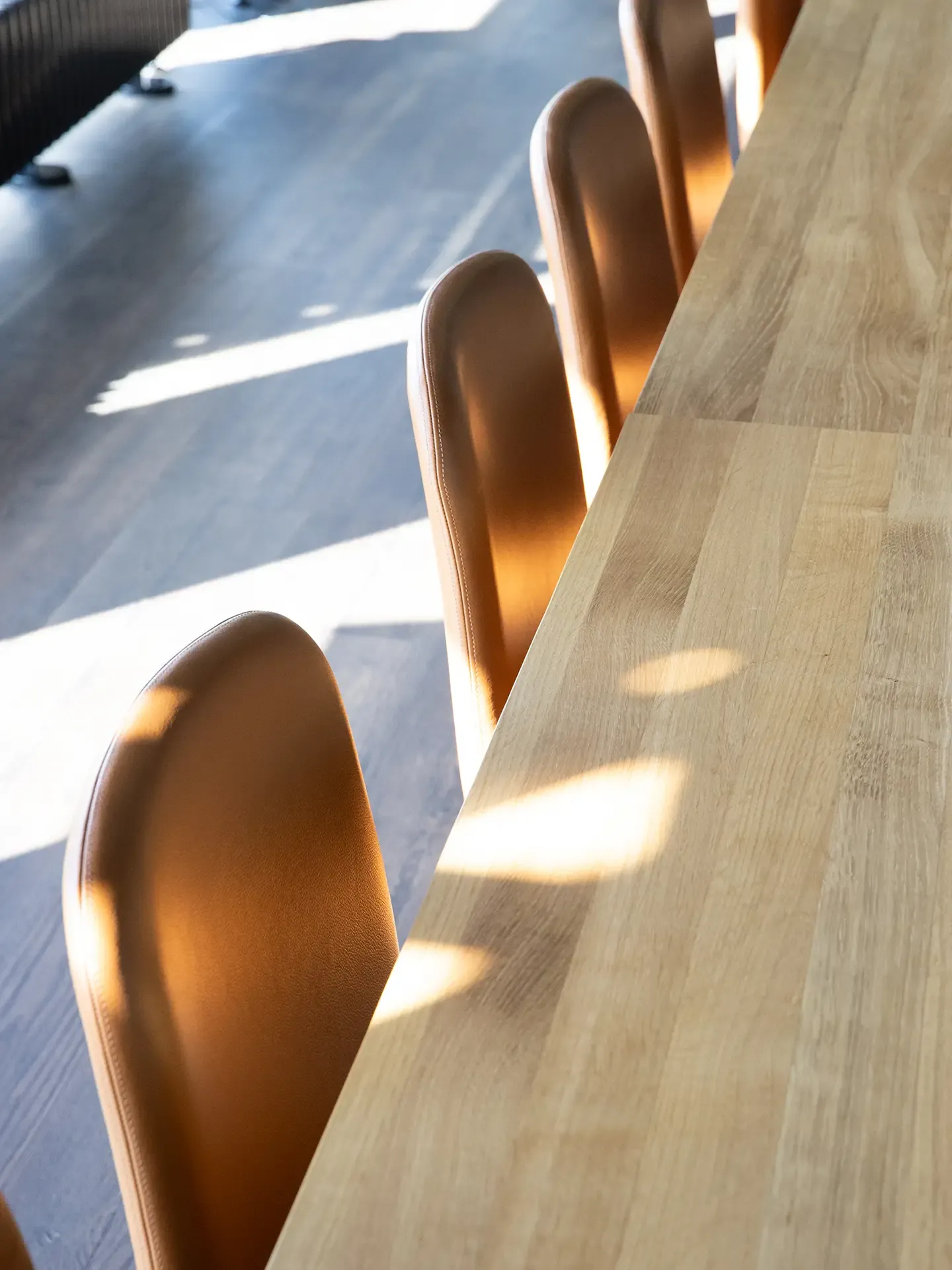Close-up of cognac leather conference chairs and oak table, highlighting craftsmanship in modern showroom design.