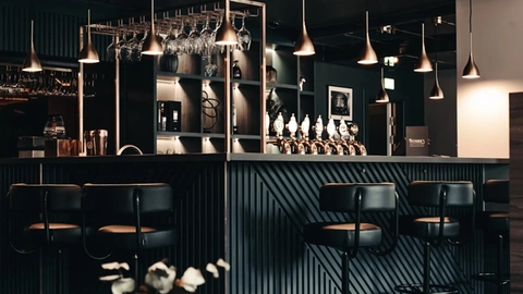 Luxury bar counter design featuring dark wood paneling and brass pendant lights at Richards Bar, Hotel Royal.